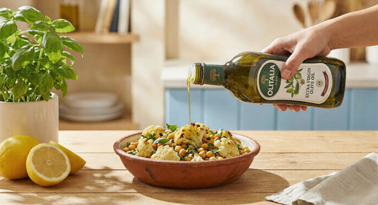 Golden Olitalia Extra Virgin Olive Oil being drizzled over a heart-healthy bowl of roasted chickpeas and cauliflower, garnished with fresh Italian herbs on a rustic wooden table.
